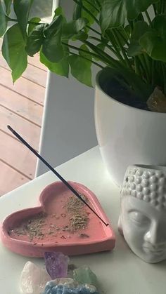 a white buddha statue next to a pink heart shaped tray with stones and a plant