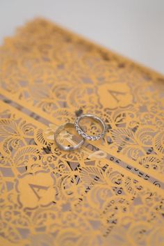 two wedding rings sitting on top of a yellow and gray paper with intricate lace design