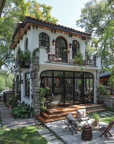 a large white house with lots of windows and plants on the front porch, surrounded by greenery