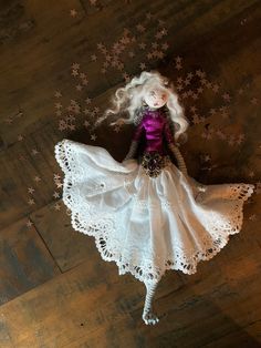 a doll is laying on the floor wearing a white dress and purple top with stars around it