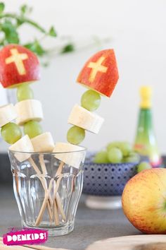 apples, grapes and marshmallows are arranged on sticks in a glass cup