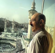 an old man standing in front of a window looking out at the city below him