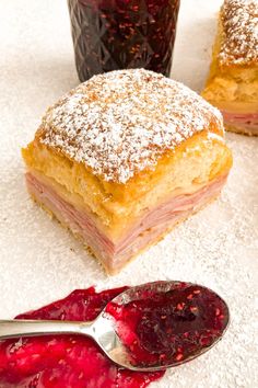 powdered sugar and jelly pastries on a white surface with a spoon next to them