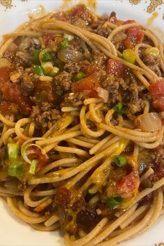 a white plate topped with spaghetti and meat covered in sauce, onions, peppers and cheese