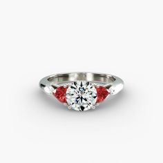 a white gold ring with two red stones on the side and a diamond in the middle