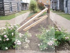 a wooden gate in the middle of some flowers and plants on the side of an old building