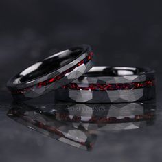 two wedding bands with red and black diamonds on them, sitting next to each other