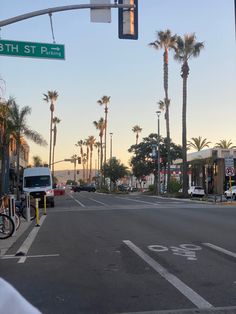 an empty street with palm trees on both sides and a traffic light hanging over the road