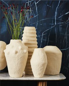 three white vases sitting on top of a table next to a planter with flowers in it