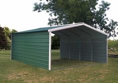 a green and white garage sitting in the middle of a grass covered field next to a tree