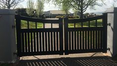 a black gate in front of a house with trees and grass on the other side