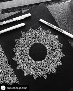 some markers and pens are sitting on top of a black paper with an intricate design