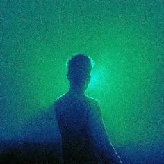 a man standing in the dark with his back turned to the camera and green light behind him