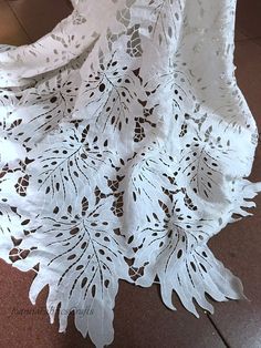 a white tablecloth with leaves on it is sitting on the floor in front of a window