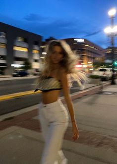 a woman is walking down the street with her hair blowing in the wind while wearing white pants