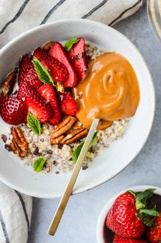 a bowl filled with oatmeal, strawberries and pecans next to a spoon