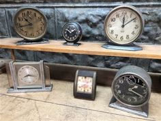 four clocks are sitting on a shelf in front of a marble wall and clock faces