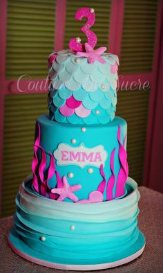 a three tiered cake decorated with pink and blue under the sea themed icing