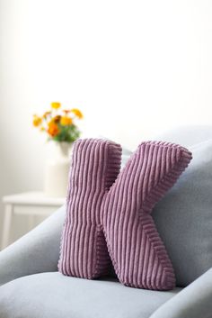 two purple pillows sitting on top of a gray couch next to a vase with flowers