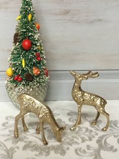 two metal deer figurines next to a small christmas tree on a tablecloth