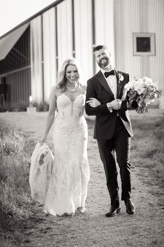 the bride and groom are walking down the path in front of their barn at this farm wedding