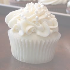 cupcakes with white frosting and sprinkles sitting on a table