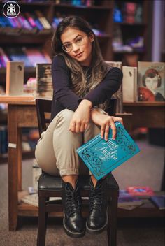 a woman sitting on top of a chair next to a table with an open book