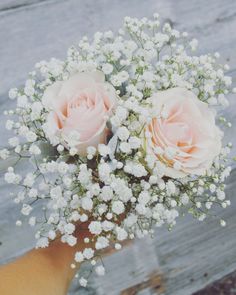 a bouquet of pink roses and baby's breath in someones hand on a wooden surface