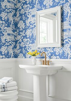 a bathroom with blue and white wallpaper, gold faucet, sink and mirror