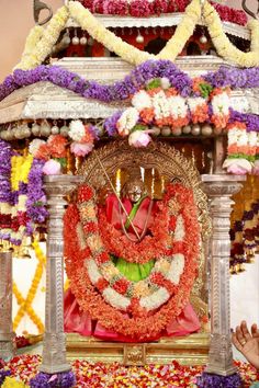 an idol is displayed in front of a stage decorated with flowers and garlands on it