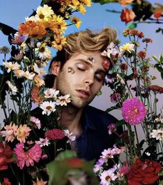 a black and white photo of a man with his eyes closed surrounded by wildflowers