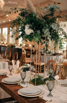 the centerpieces on this table are tall, with greenery and white flowers