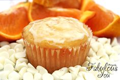 an orange cupcake with frosting surrounded by white chocolate chips and sliced oranges