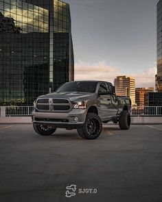 a ram truck parked in front of some tall buildings at dusk with the lights on