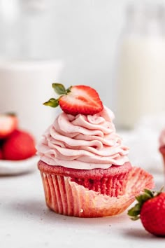 a strawberry cupcake with pink frosting and strawberries on the table next to it