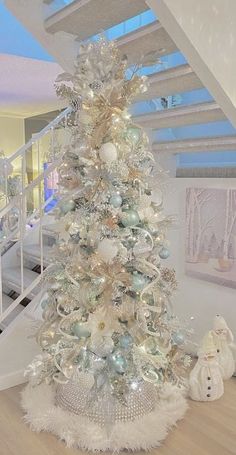 a white christmas tree with silver ornaments and lights on it in front of a staircase