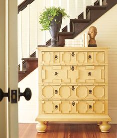 a yellow dresser sitting in the middle of a wooden floor next to a stair case