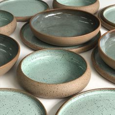 many bowls and plates are stacked on top of each other, with speckled glazes