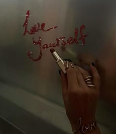 a woman writing on the side of a refrigerator with red letters that spell love yourself