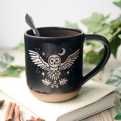 a black coffee mug with an owl design on it and some cinnamons around it