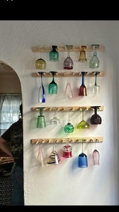 there are many different colored glass vases on the wall and hanging from wooden shelves