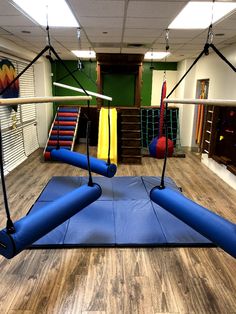 an empty gym with blue and yellow mats on the floor, swings and ladders hanging from the ceiling