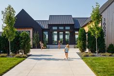 two girls are walking towards the front door of a modern house with black shingles