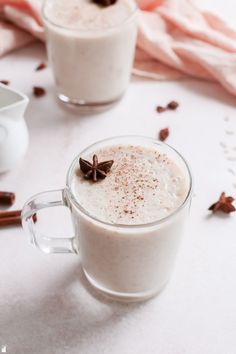 two mugs filled with hot chocolate drink on top of a white tablecloth next to cinnamon sticks