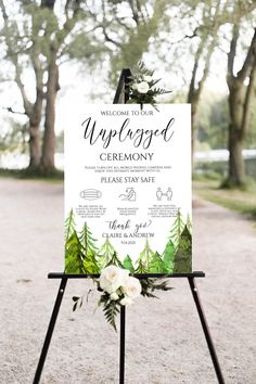 a welcome sign with greenery and white flowers on it in front of some trees