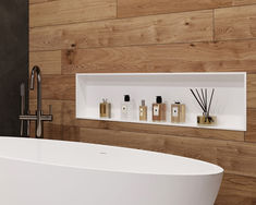 a white bath tub sitting next to a wall mounted shelf filled with bottles and reeds