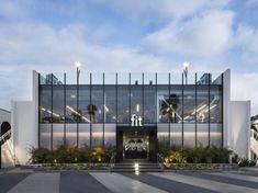 the front entrance to an office building with glass walls and palm trees on either side