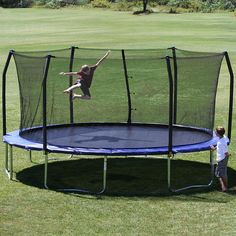 a young boy is jumping on a trampoline in the grass while another child watches