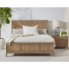 a bed with white sheets and pillows in a room next to a potted plant