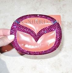 someone is holding up a pink brooch with purple crystals on it's face